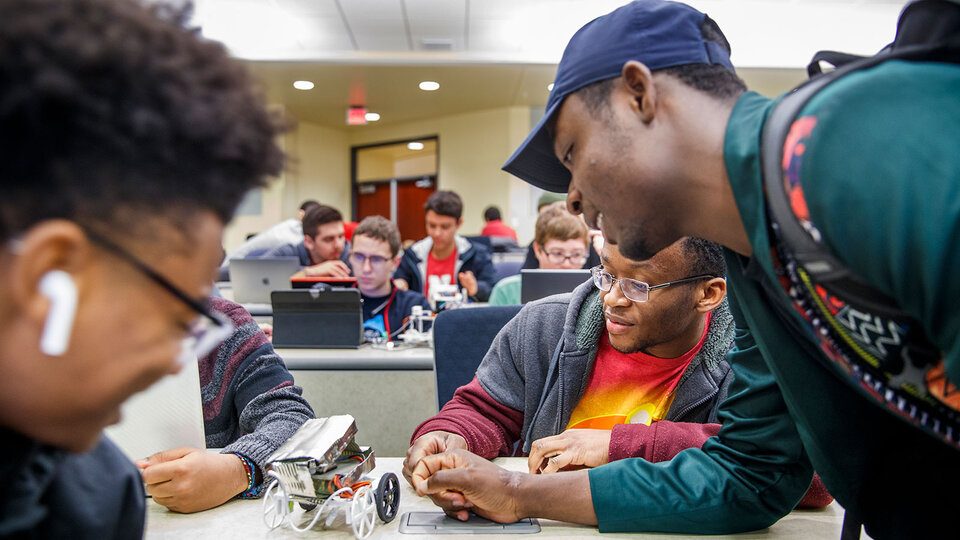 ECE students huddle around a small mechanical vehicle they are building.