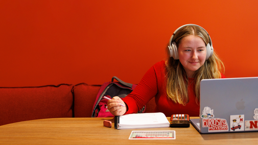 student with headphones, open laptop and notebook with pencil in hand at a table