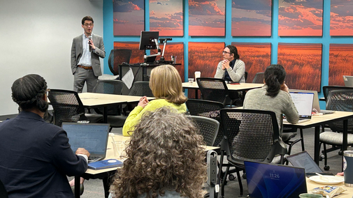 Ben Lee speaking to seated attendees in a classroom with a blue wall and sunset artwork.
