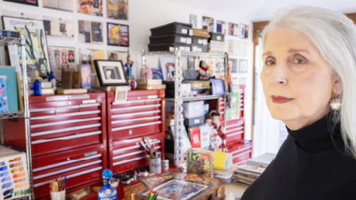 Karen Blessen in a studio with shelves, red toolboxes, art supplies, and framed artworks in the background.