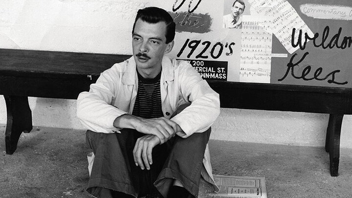 A black-and-white photo of artist Weldon Kees sitting on the ground.