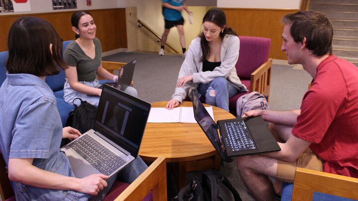 Four students sitting around a table with laptops.