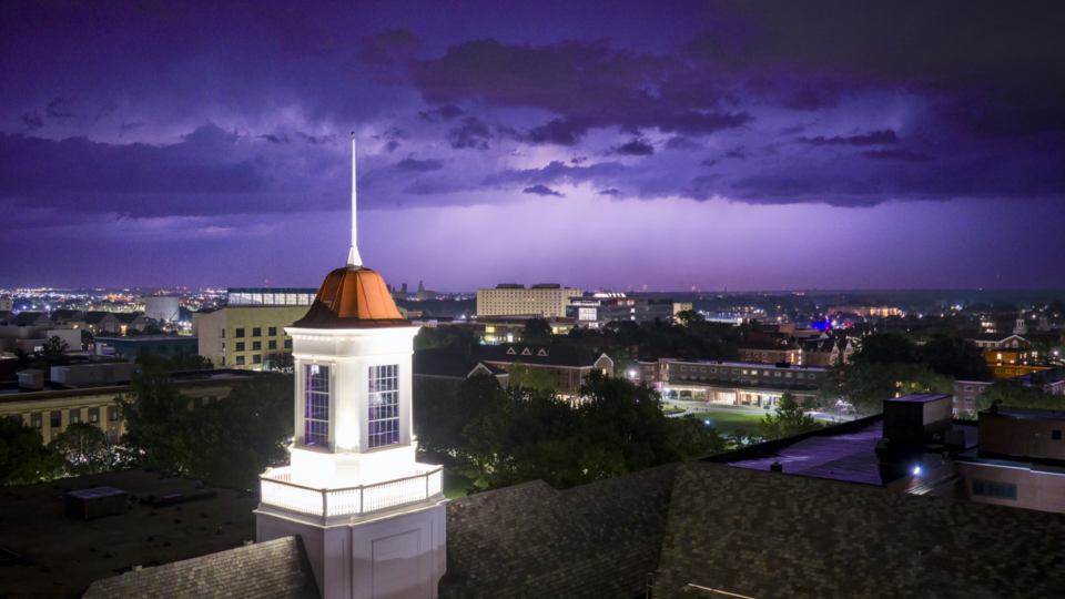Cupola against a stormy purple sky over city buildings at night.