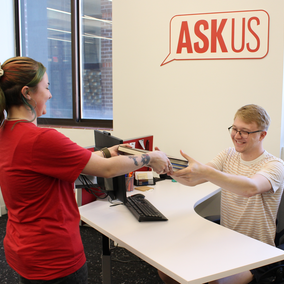 Student handing books to an ASKus person sitting behind a desk