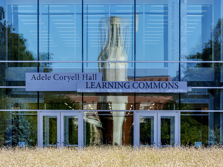 A reflection of the Green Point sculpture, Mueller Tower and Coliseum are distorted by the windows on the north side of the Adele Hall Learning Commons.