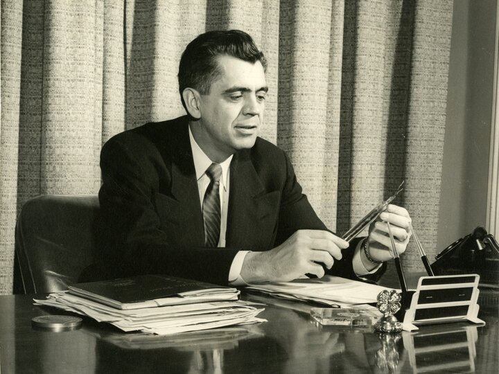 Clifford Hardin seated at a desk looking at documents.