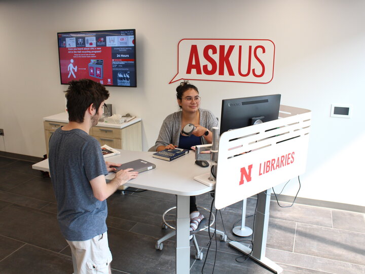Photo of a student checking out a book at an ASKus service desk.