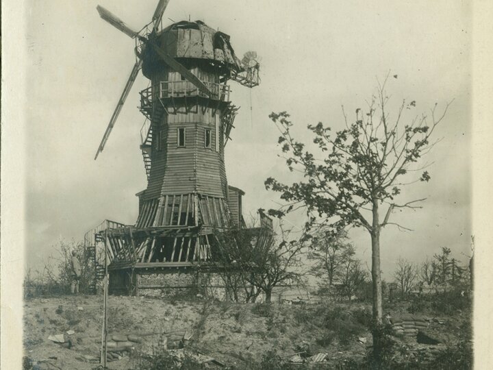 A man stands at the base of a large wooden windmill in a rural landscape.