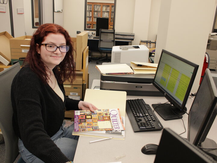 Student worker sitting at a computer working on quilt archival materials.