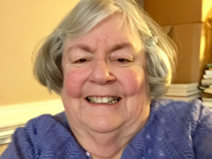 Jane Crabill with short gray hair wearing a purple patterned top indoors.