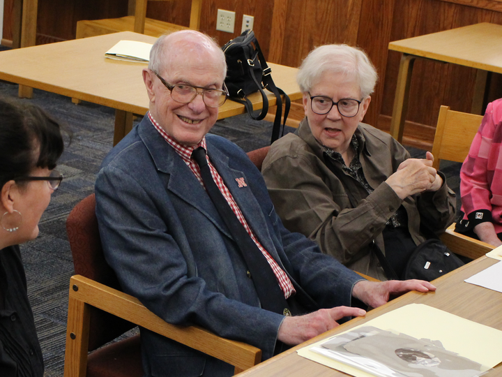Jim and Connie Thorson seated at a table, smiling and talking in a library-like setting.