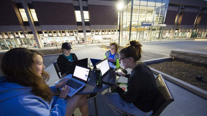 Four students study in the dusk light outside the Adele Hall Learning Commons.