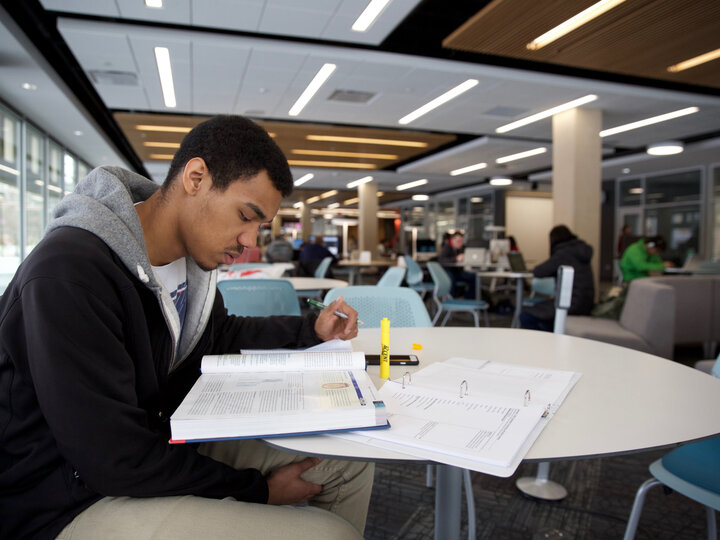 Student studying at a table with books and binders on the table.
