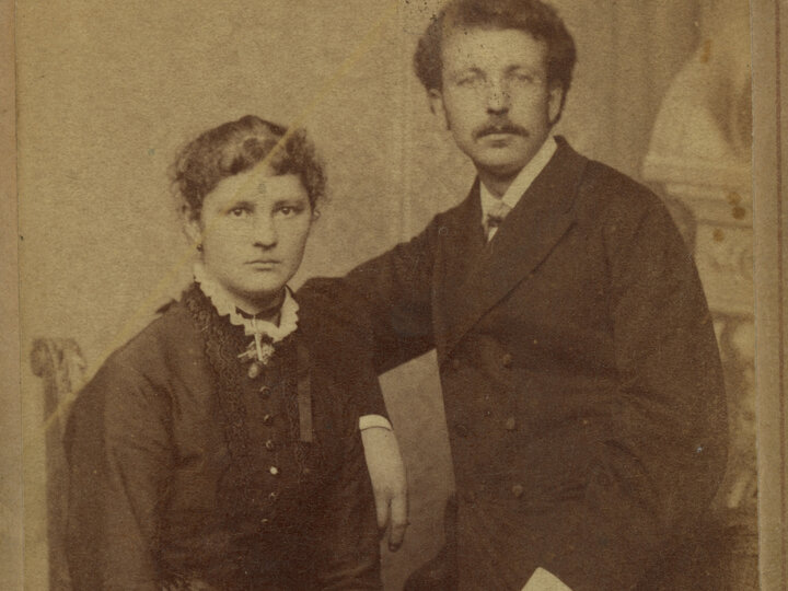 A man and woman sitting, unsmiling for a photo.