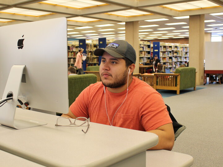 Student with earbuds in looking at a monitor.