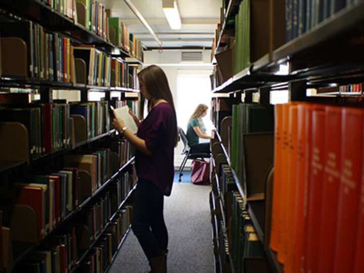 Student standing in the stacks with a book in hand.